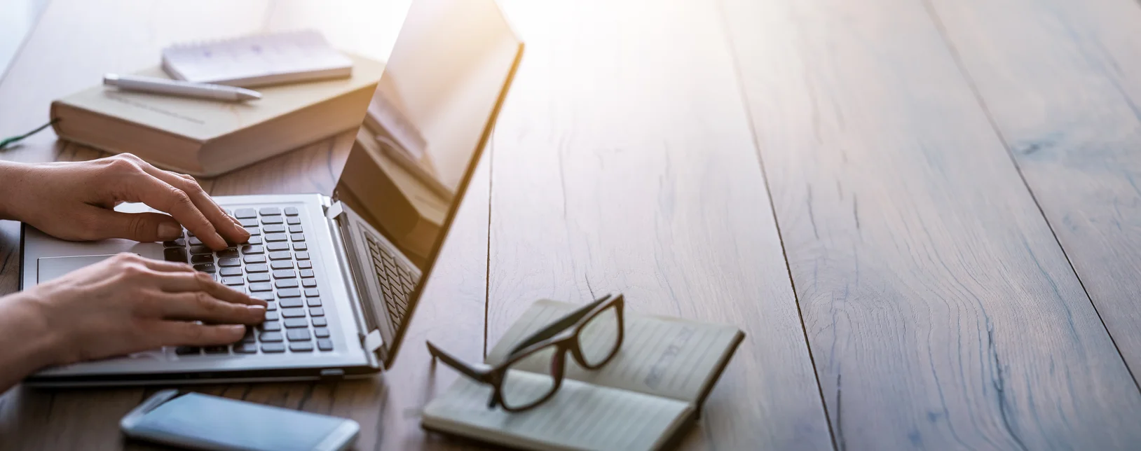 man using laptop with book and glasses on desk
